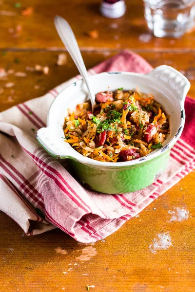 Traditional polish food. Bigos, stewed cabbage with carrot, onion, green lentil and pork meat sausages in a pot on a wooden table, selective focus. German cuisine. Comfort food.