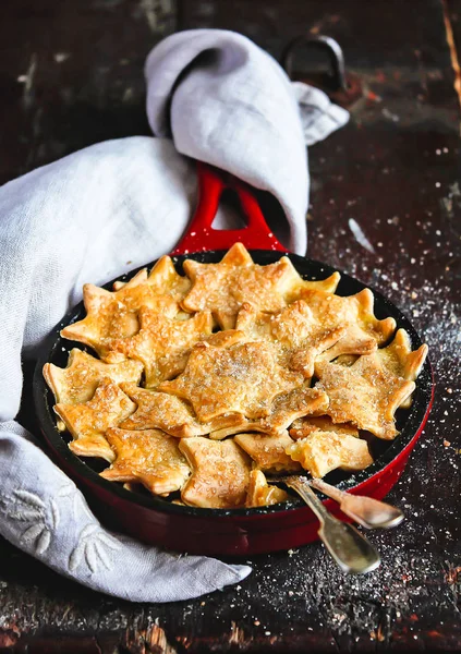 Sweet pie with apple fruit and cinnamon covered with sweet short crust pastry in the shape of stars dusted with brown sugar on a wooden table, selective focus. American apple pie. Sweet food.