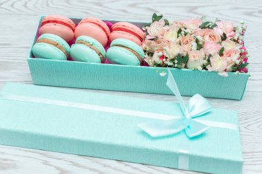 Çiçekler ve badem kurabiyeleri hediye mavi kutu beyaz ahşap arka planda izole.