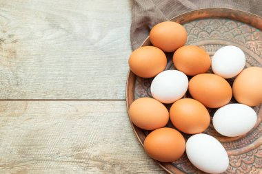 Ahşap arka planda bir tabakta beyaz ve kahverengi yumurtalar. Paskalya kompozisyonu, model.
