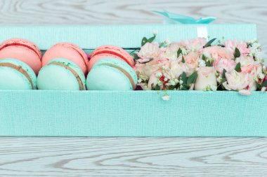 Pembe, mavi çiçekler ve beyaz ahşap arka planda hediye kutusunda kurabiyeler. Hediye olarak gül ve tatlı, bahar bayrağı..