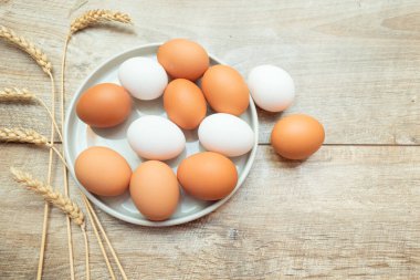 Ahşap arka planda, tabakta çiğ kahverengi ve beyaz yumurtalar. Paskalya kompozisyonu, modelleme, üst görünüm, en düşük biçim.