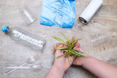 Plastik mutfak gereçleri, şişe, selofan çanta, kutu, bardak. Ahşap arka planda yeşil bitki filizi tutan kadın. Çevre dostu, organik, ekoloji, sıfır atık, geri dönüşüm konsepti. en üstteki görünüm