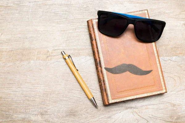 Happy Fathers day holiday concept, greeting card, notebook with pen, glasses and mustache on a rustic wooden background with copy space.