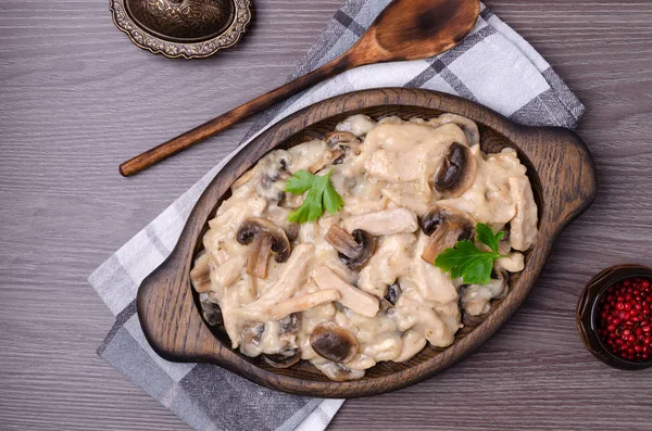 Stewed meat slices with mushrooms in a dish on a wooden background. Selective focus.