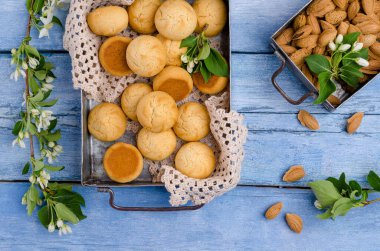 Mavi ahşap arka planda, dalları çiçek açmış bademli yuvarlak kurabiyeler. Seçici odak.
