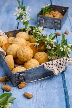 Mavi ahşap arka planda, dalları çiçek açmış bademli yuvarlak kurabiyeler. Seçici odak.