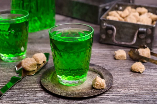 Green liquid in a glass with sugar cubes on a dark wooden background. Selective focus.