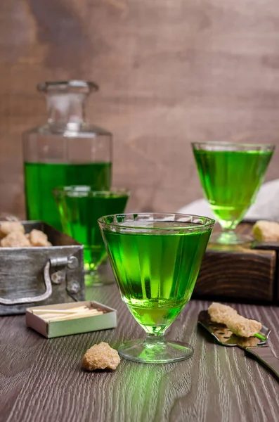 Green liquid in a glass with sugar cubes on a dark wooden background. Selective focus.