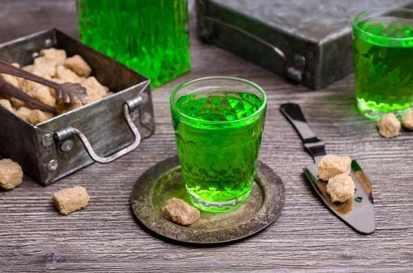 Green liquid in a glass with sugar cubes on a dark wooden background. Selective focus.