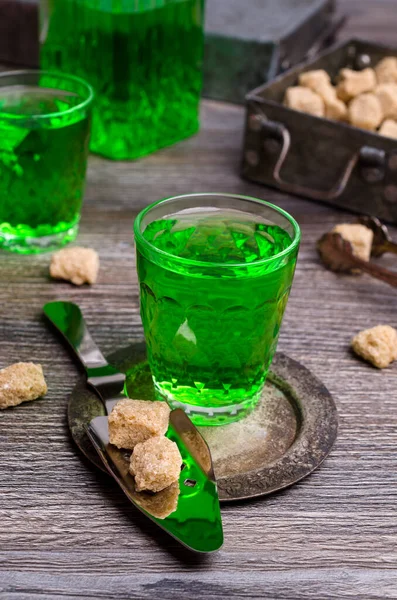 Green liquid in a glass with sugar cubes on a dark wooden background. Selective focus.