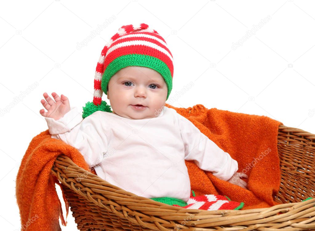 Little baby girl sitting in rustic stroller saluting. Child dressed in homemade knitted wear for cold weather as a Christmas dwarf costume. 