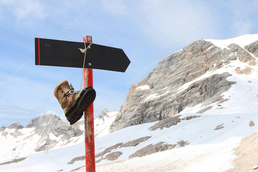 Old hiking boot on empty signpost in snowy alpine landscape 
