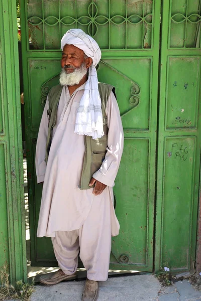 Afghanischer Mann steht in traditionellem Outfit und posiert vor dem Tor seines Hauses. — Stockfoto