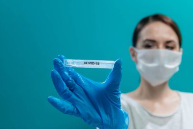 Tıbbi maskeli ve mavi eldivenli bir kız üzerinde virüs olan bir test tüpü gösteriyor.