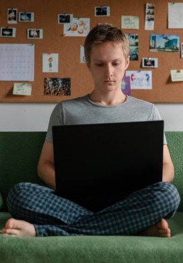 Adam kanepede oturuyor ve evden bilgisayarla çalışıyor. Dikey olarak.