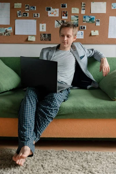 The boss in a jacket is sitting on the couch and holding a meeting on a laptop, sprawled on the couch