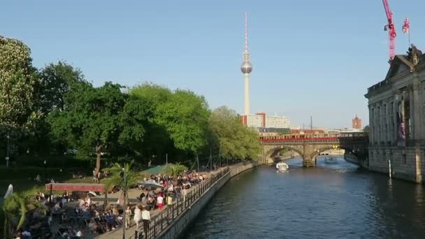 Personas sentadas bajo el sol de la noche en la cafetería del río Spree en Berlín. En el fondo torre de televisión de Alexanderplatz . — Vídeo de stock