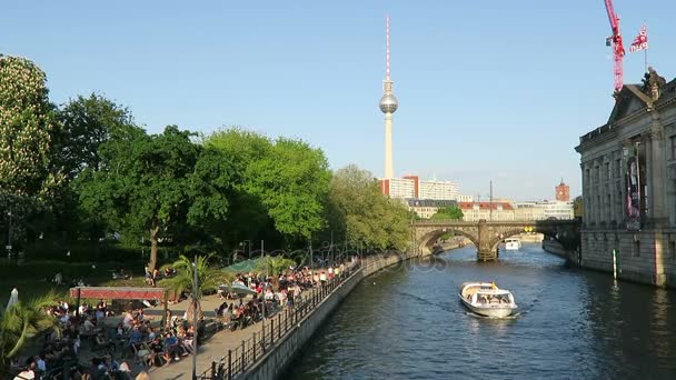 Personas sentadas bajo el sol de la noche en la cafetería del río Spree en Berlín. En el fondo torre de televisión de Alexanderplatz . — Vídeos de Stock