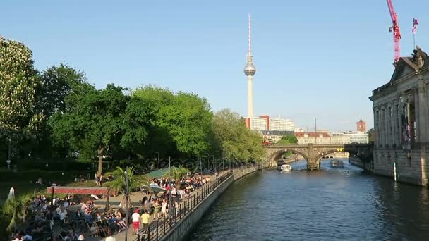 Personas sentadas bajo el sol de la noche en la cafetería del río Spree en Berlín. En el fondo torre de televisión de Alexanderplatz . — Vídeos de Stock