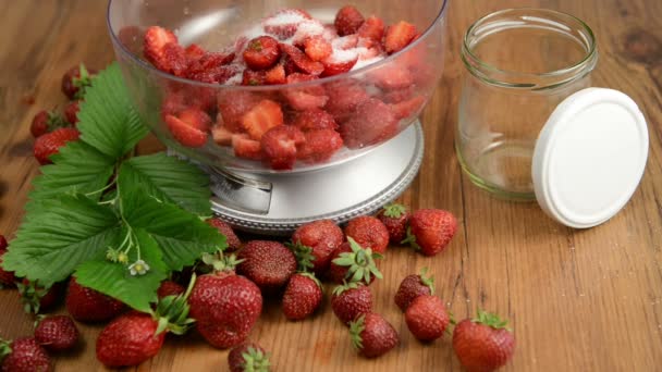Erdbeeren in Schüssel auf der Gewichtswaage mit Zucker. Blatt und Blütenkopf auf einem Holztisch. Marmelade kochen. — Stockvideo