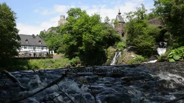 Cascada del río Elz con una pequeña iglesia en un puente y un antiguo molino de agua de madera. El río fluye a lo largo de la aldea Monreal y el castillo Burg Eltz. (Eifel, Alemania ) — Vídeo de stock