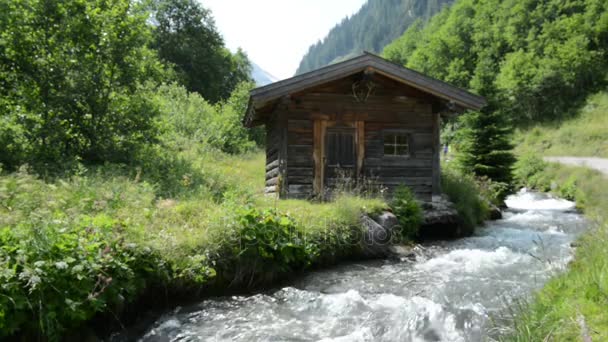 Wanderer gehen an einer kleinen Almhütte am Bachwasser im Zillertal vorbei). — Stockvideo