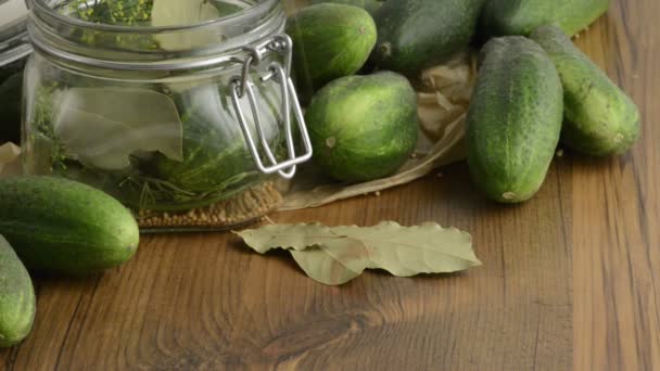 Gewürze wie Dill, Chili, Senfkörner fallen in ein Einmachglas auf einem Tisch. einen Korb mit grünen Gurken beiseite legen — Stockvideo