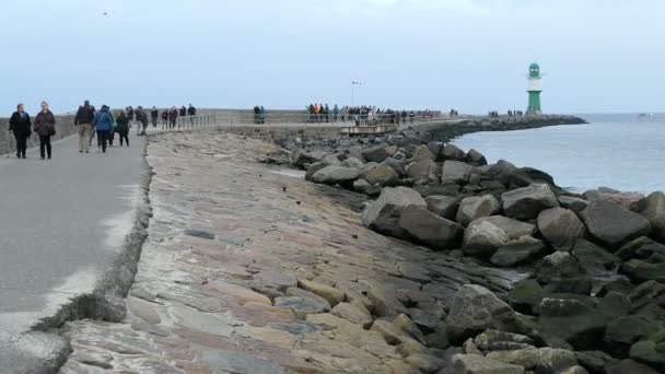 Gente caminando por el paseo marítimo de Warnemuende hacia el faro en el mar Báltico . — Vídeos de Stock