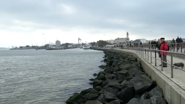 People walking along the promenade of Warnemuende towards the lighthouse on Baltic sea. — Stock Video