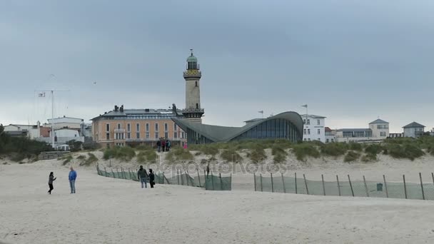 人们沿着海滩漫步在 Warnemuende。在背景灯塔和茶壶房子. — 图库视频影像