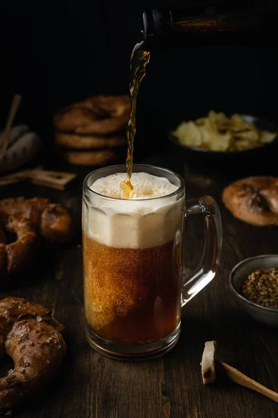 Bière versant dans le verre avec bretzels, bratwurst et collations sur rus — Photo