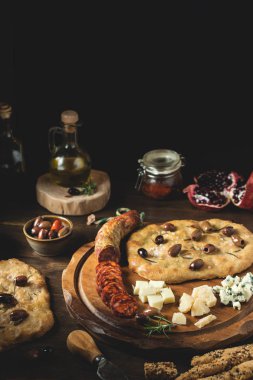 Focaccia, zeytinyağı, kurutulmuş domates, zeytin, peynir, şarap, koyu ahşap arka planda domuz sosisi, fotokopi alanı