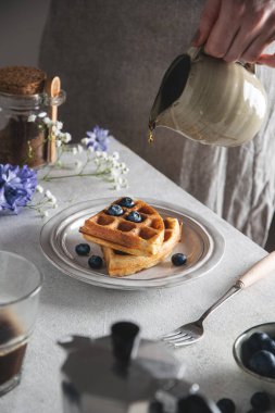 Gri masada taze pişmiş Belçika waffle 'ı, ballı ve yabanmersinli.