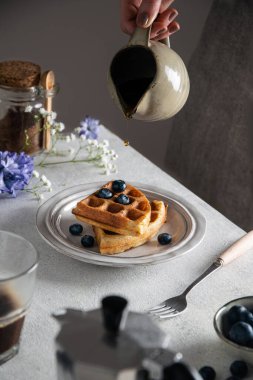 Gri masada taze pişmiş Belçika waffle 'ı, ballı ve yabanmersinli.