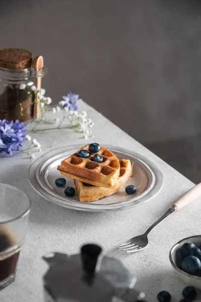 Gri masada taze pişmiş Belçika waffle 'ı, ballı ve yabanmersinli.