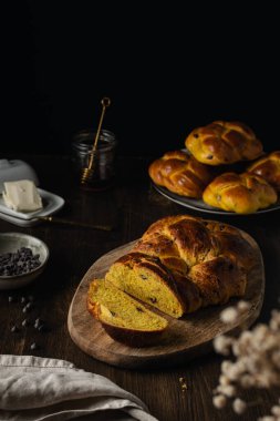 Çikolata parçacıklı taze brioche, bal, tereyağı, siyah ahşap arka planda süt.