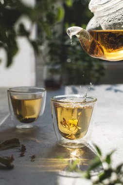 Yaz ıhlamur çiçeği çayı, beyaz ışık masasına serpiştirilmiş, arka planda bokeh yaprakları olan.