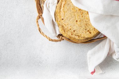 Mutfak havlusuyla kaplı hasır bir tepside Meksika mısır tortillası yığını.