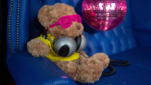 Bruine Teddybeer Pluizig Speeltje Zonnebril Hoofdtelefoon Met Discobal Sofa Achtergrond — Stockvideo