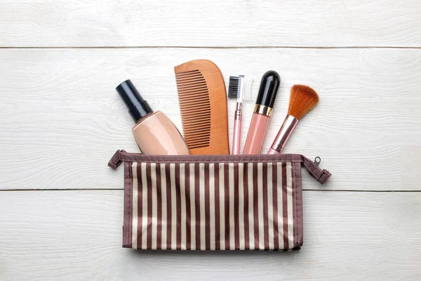 makeup kit. Women\'s cosmetics in a cosmetic bag and makeup brushes on a white wooden background. top view