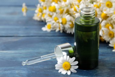 Tıbbî papatya çayı ve papatya çayı özü şişede. Papatya çiçeklerinden yağ. Aromaterapi. Bir uyuşturucu. Mavi ahşap bir masada. yakın plan