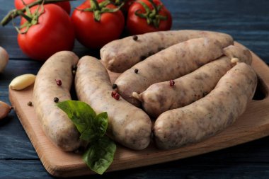 Çiğ sosisler kızarma için hazırlandı ve malzemeler yemek, sarımsak, domates, fesleğen ve mavi arka planda..