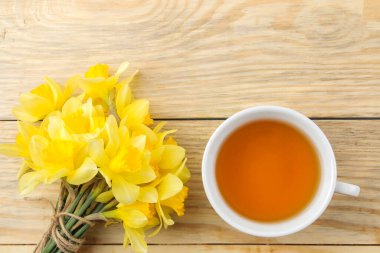 Bahar çiçekleri, sarı nergisler ve doğal ahşap arka planda bir fincan çay. metin için yer