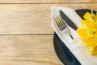 Masa seti, bahar çiçekleri, sarı nergisler. Tabak, bıçak ve çatal doğal ahşap bir masa üzerinde. en üstteki görünüm