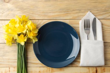 Masa seti, bahar çiçekleri, sarı nergisler. Tabak, bıçak ve çatal doğal ahşap bir masa üzerinde. en üstteki görünüm