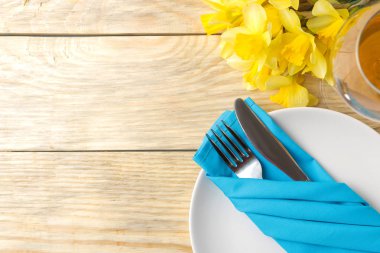 Masa seti, bahar çiçekleri, sarı nergisler. Tabak, bıçak ve çatal, doğal ahşap bir masada bir bardak şarap. Romantik yemek. en üstteki görünüm