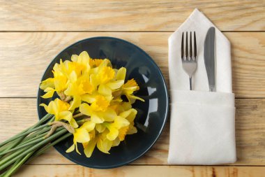 Masa seti, bahar çiçekleri, sarı nergisler. Tabak, bıçak ve çatal doğal ahşap bir masa üzerinde. en üstteki görünüm