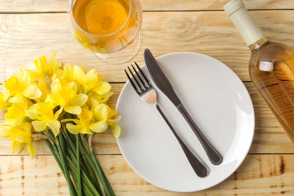 桌上摆满了春花 黄色的水仙花 一杯葡萄酒放在一张天然的木制桌子上 浪漫的晚餐顶部视图 — 图库照片