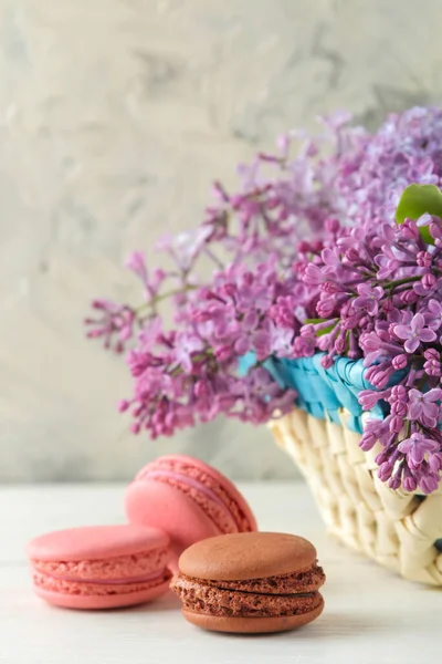 Frühlingsblumen Blühende Fliederzweige Weidenkorb Und Makronenkuchen Auf Hellem Betongrund — Stockfoto